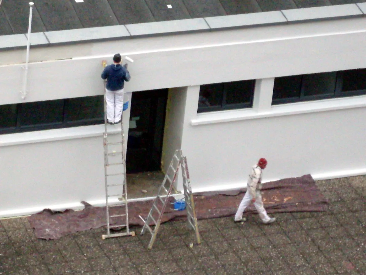Fassadenmaler traegt ein Motiv mit dem Pinsel auf eine Hauswand auf